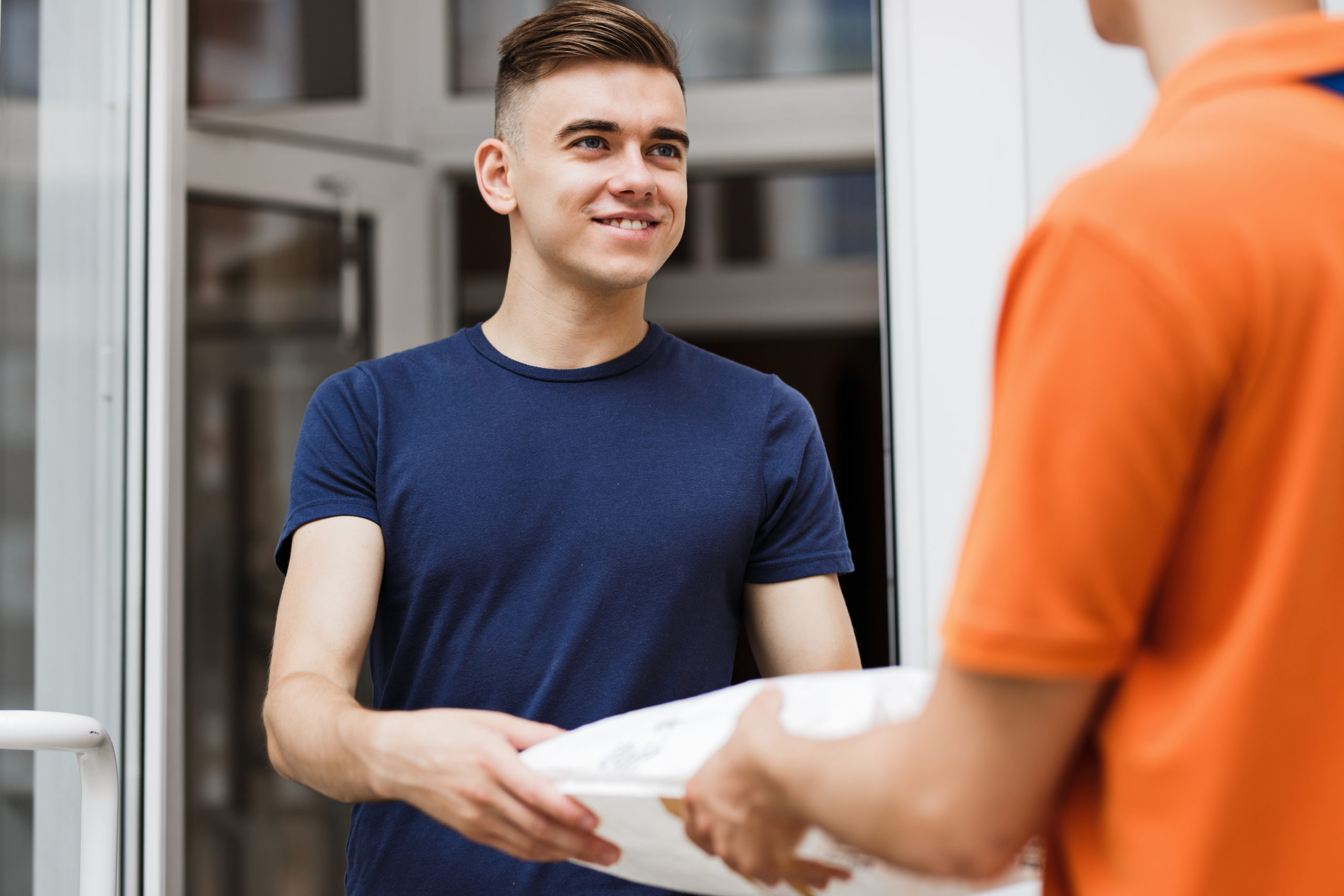 A person wearing an orange T-shirt is delivering a parcel to a satisfied client. Friendly worker, high quality delivery service