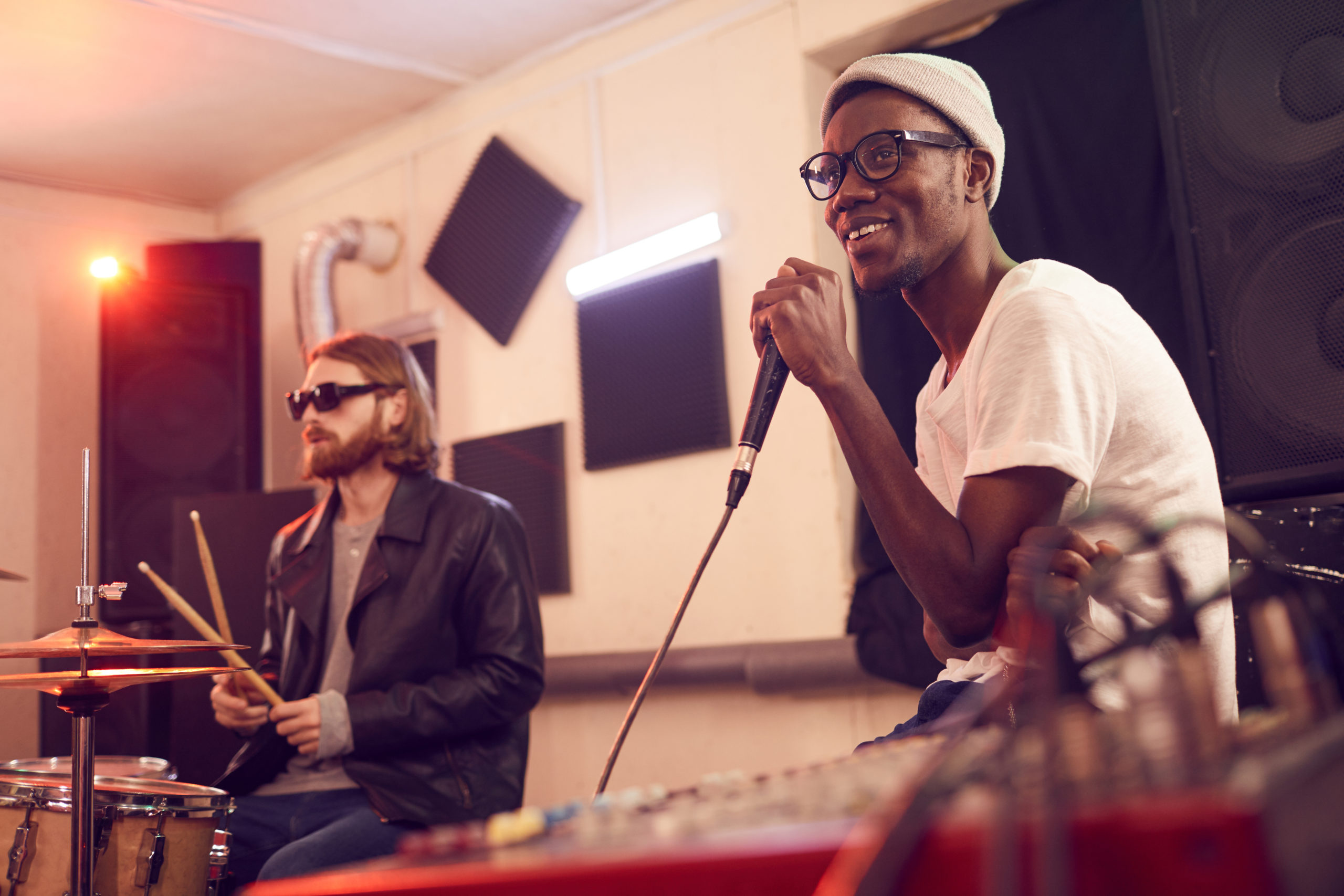 Portrait of contemporary African-American man singing to microphone and smiling happily during rehearsal or concert in music studio, copy space